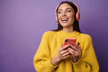 Kulaklık takan, elinde cep telefonu olan mutlu genç bir kadın.