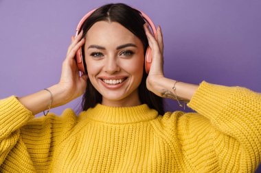 Kulaklıklı, menekşe rengi duvar arkasında müzik dinleyen mutlu genç bir kadın.