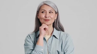 Memnun bir yaşlı kadın, stüdyodaki gri bir duvarın üzerinde duran bir şeyin hayalini kuruyor.