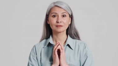 Odaklanmış yaşlı bir kadın kameraya bakıyor sonra stüdyodaki gri bir duvarın ardında kendini şaşkın ve mutlu hissediyor.