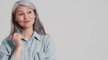 Mutlu bir yaşlı kadın, stüdyodaki gri bir duvarın üzerinde duran yan tarafı işaret ediyor.