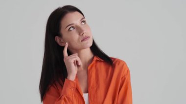 Ciddi bir kadın stüdyodaki gri duvarın üzerinde duran bir şeyi düşünüyor.