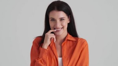 Gülen bir kadın kameraya bakıyor. Stüdyodaki gri duvarın üzerinde tek başına duruyor.