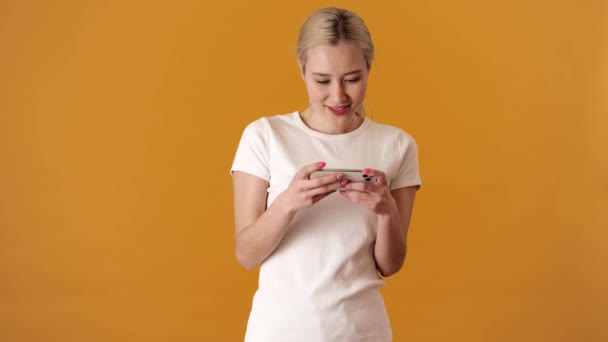 Een Gepassioneerde Blonde Aziatische Vrouw Spelen Telefoon Terwijl Een Oranje — Stockvideo