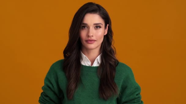 一位穿着绿色毛衣和衬衫 站在橙色工作室里的年轻女子非常惊讶 — 图库视频影像