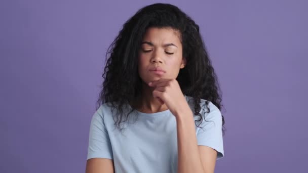 一个穿着T恤衫 心烦意乱 卷曲头发的年轻非洲女人站在一个紫色的工作室里 脑子里在想什么 还因为缺乏创意而握手 — 图库视频影像