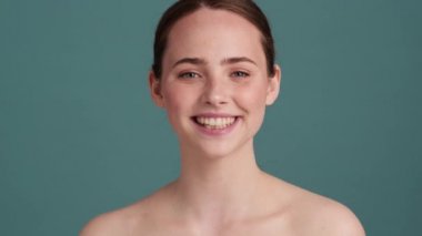 Memnun bir yarı çıplak kadın kameraya göz kırpıyor. Stüdyonun gri duvarında tek başına duruyor.