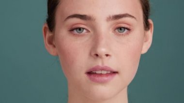 Güzel bir kadının yakın plan görüntüsü, stüdyodaki gri duvarın üzerinde kameraya poz verirken yüzüne dokunuyor.