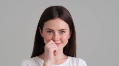 Temel t-shirt giyen çekici bir kadın kameraya bakıyor. Stüdyonun gri arka planında tek başına duruyor.