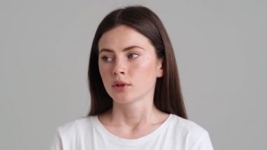Temel tişört giyen üzgün ve üzgün bir kadının yakın plan görüntüsü stüdyonun gri arka planında tek başına kameraya bakıyor.