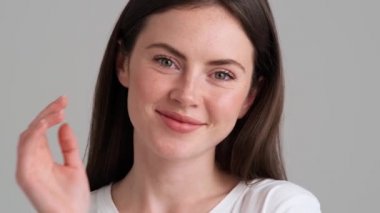 Çekici bir kadının yakın çekim görüntüsü kameraya poz verirken saçına dokunuyor. Stüdyonun gri arka planında izole bir şekilde duruyor.