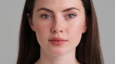 Güzel bir kadının yakın çekim görüntüsü stüdyodaki gri arka planda tek başına duran kameraya bakıyor.