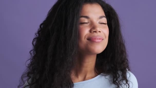 一个穿着T恤衫的快乐的非洲女人站在紫色的工作室里享受着这种味道的特写镜头 — 图库视频影像