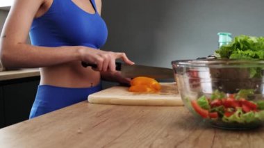Spor takım giyen sağlıklı bir sporcunun kırpılmış görüntüsü evdeki mutfakta salata yapıyor.