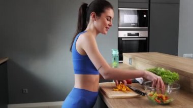 Bir sporcu kadın evde mutfakta salata yapıyor.