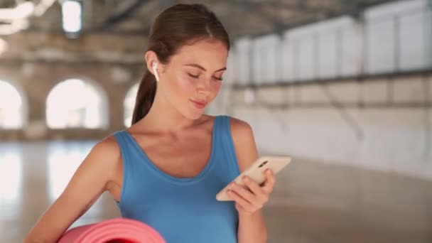 Šťastná Žena Modrém Sportovním Obleku Pomocí Svého Smartphonu Drží Podložku — Stock video