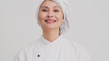 Memnun bir aşçı kadın stüdyodaki gri duvarın arkasında duran kameraya hoş bir jest yapıyor.