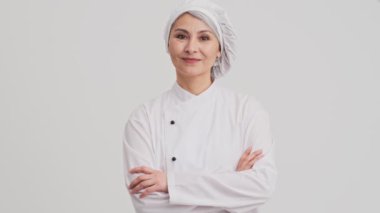 Güzel bir aşçı kadın stüdyodaki gri duvarın arkasında dikilip duruyor.