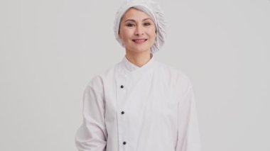 Güzel bir aşçı kadın, stüdyodaki gri duvarın üzerinde tek başına baş parmak hareketi yapıyor.