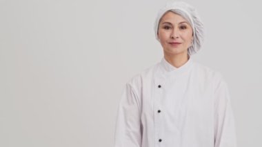 Memnun bir aşçı kadın stüdyodaki gri duvarın ardında kendine güvenen bir poz veriyor.