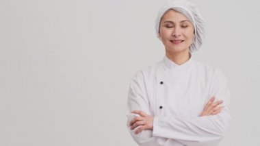 Gülümseyen bir aşçı kadın stüdyodaki gri duvarın diğer tarafını işaret ediyor.