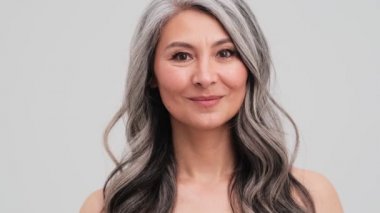 Mutlu, yaşlı bir kadın, gri duvarın üzerinde durmuş, gülüşünü gösteriyor.