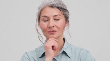 Düşünen yaşlı bir iş kadınının yakın plan görüntüsü stüdyodaki gri duvarın üzerinde tek başına duran bir fikirle ortaya çıkıyor.