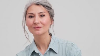 Olumlu bir iş kadınının yakın plan görüntüsü stüdyodaki gri duvarın üzerinde el sallıyor.