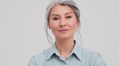 Gülümseyen yaşlı bir iş kadınının yakın çekim görüntüsü stüdyodaki gri duvarın üzerinde izole bir şekilde duruyor.