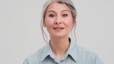 Mutlu yaşlı bir iş kadınının yakın plan görüntüsü stüdyodaki gri duvarın üzerinde tek başına durmaktan mutluluk duyuyor.