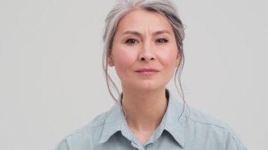 Hayal kırıklığına uğramış yaşlı bir iş kadınının yakın plan görüntüsü stüdyodaki gri duvarın üzerinde tek başına duruyor.