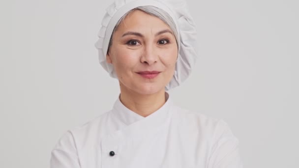一位面带微笑的资深女厨师正对站在工作室灰墙上的摄像机眨眼 — 图库视频影像