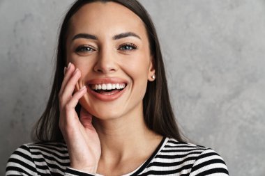 Gri arka planda izole edilmiş uzun saçlı, güzel, gülümseyen esmer bir kadına yakın durun.