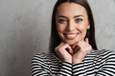 Gri arka planda izole edilmiş uzun saçlı, güzel, gülümseyen esmer bir kadına yakın durun.