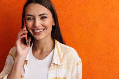 Gri arka planda izole edilmiş cep telefonu kullanan mutlu, neşeli bir kadın.