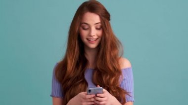 Stüdyonun mavi duvarında duran güzel bir kadın akıllı telefonunu kullanıyor.