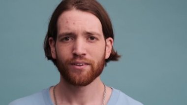 Hayal kırıklığına uğramış bir adam kameraya bakarken kafasına dokunuyor ve mavi arka planda tek başına duran bir beyin işareti göstermiyor.