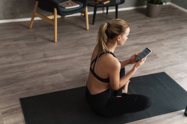 Çekici genç, sağlıklı bir sporcu. Kapalı alanda spor minderinin üzerinde otururken cep telefonu kullanıyor.