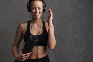 Kablosuz kulaklıklar ve spor giysileri tutan spor kıyafetleri giyen genç, gülen atletik kadın izole edilmiş.