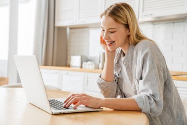 Gülümseyen ve dizüstü bilgisayar kullanan neşeli sarışın kız.