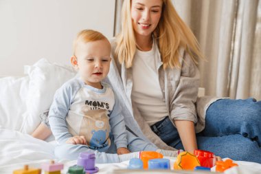 Genç anne, bebeğiyle evde yatakta oynuyor.