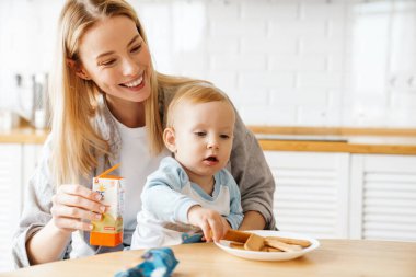 Mutlu genç anne oğlunu meyve suyu ve kurabiyelerle besliyor.