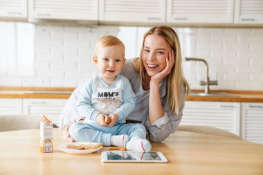 Bebeğini evde beslerken tablet bilgisayar kullanan mutlu güzel bir kadın.