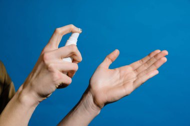 Mavi duvardan izole edilmiş el ve dezenfektan spreylerinin yakın çekimi.