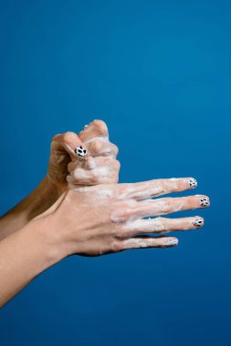 Mavi duvardan izole edilmiş sabunlu ellerin yakın çekimi.