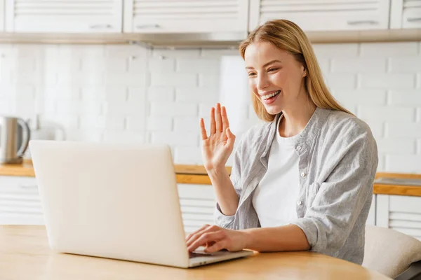 Menina Loira Alegre Acenando Mão Usando Laptop Enquanto Sentado Cozinha — Fotografia de Stock