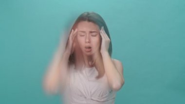 Turkuaz arka plan yüzünden baş ağrısı çeken tişörtlü esmer kadın.