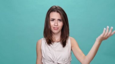 Şok olmuş esmer tişörtlü kadın aynı fikirde değil ve turkuaz arka planda kameraya bakıyor.