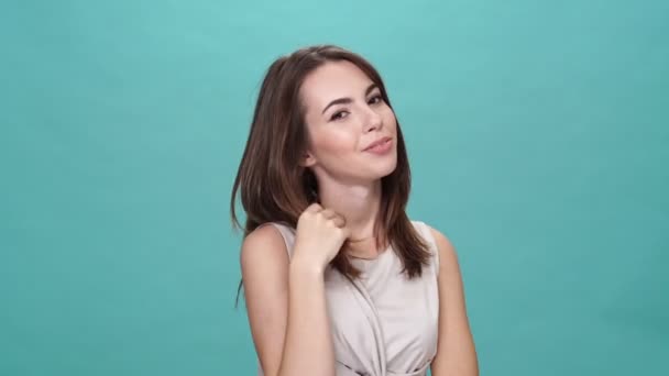 Nieśmiała Brunetka Shircie Dotykająca Włosów Patrząca Kamerę Turkusowym Tle — Wideo stockowe