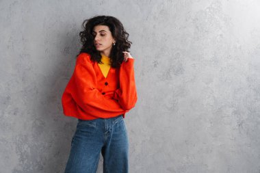 Gri arka planda yalnız poz veren kendine güvenen çekici genç bir kadın.